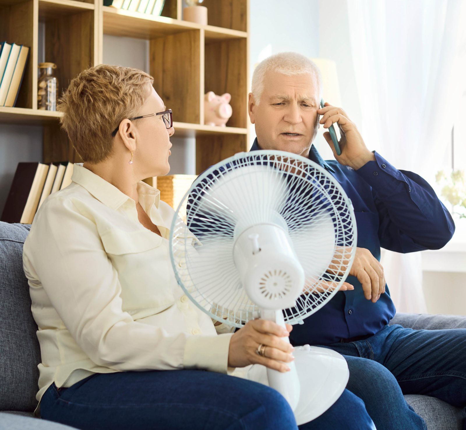 An older couple keeping cool with a fan while calling for emergency AC service in Tampa